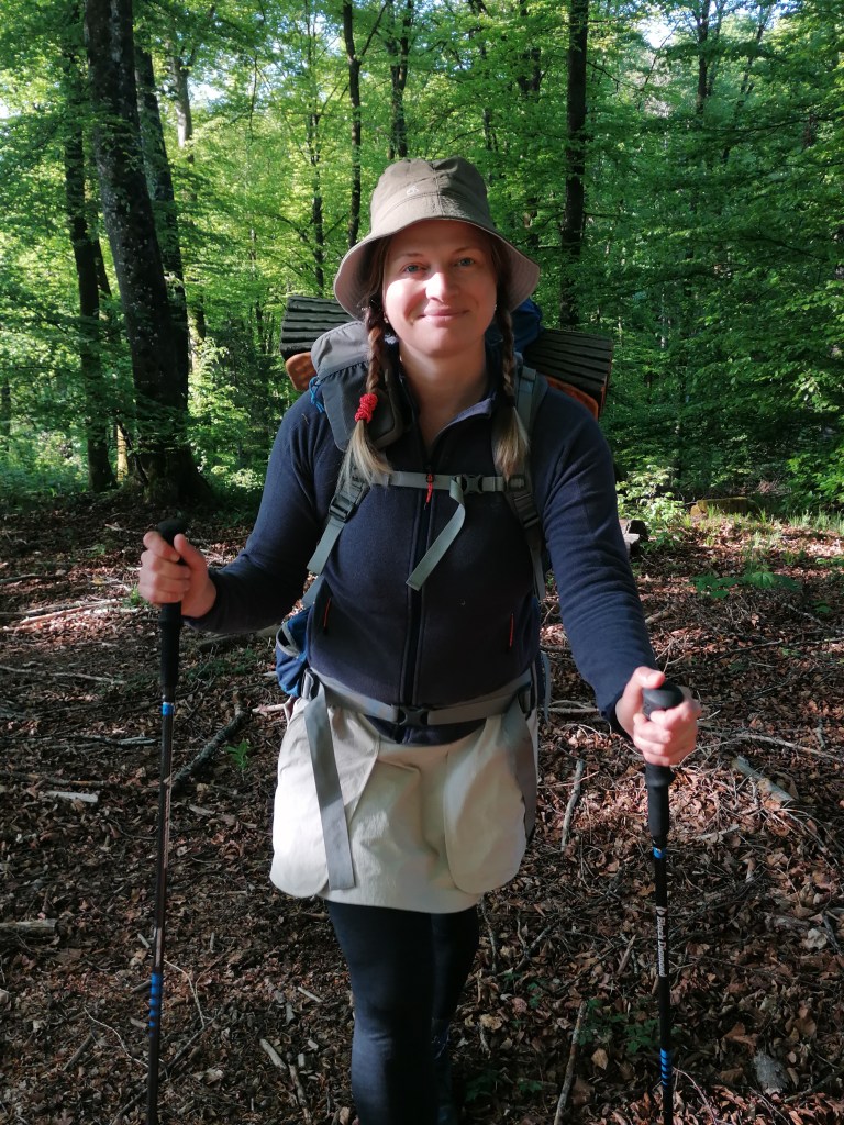 Anna Schönharting unterstützt Funkenzeit als Tourenleiterin. Sie ist auf dem Bild in im Wanderoutfit mit Rucksack und Wanderstöcken im Wald zu sehen.